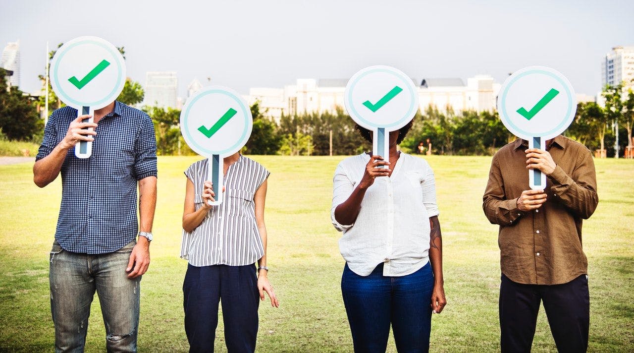 image of four individuals each holding a panel with a green tick on it