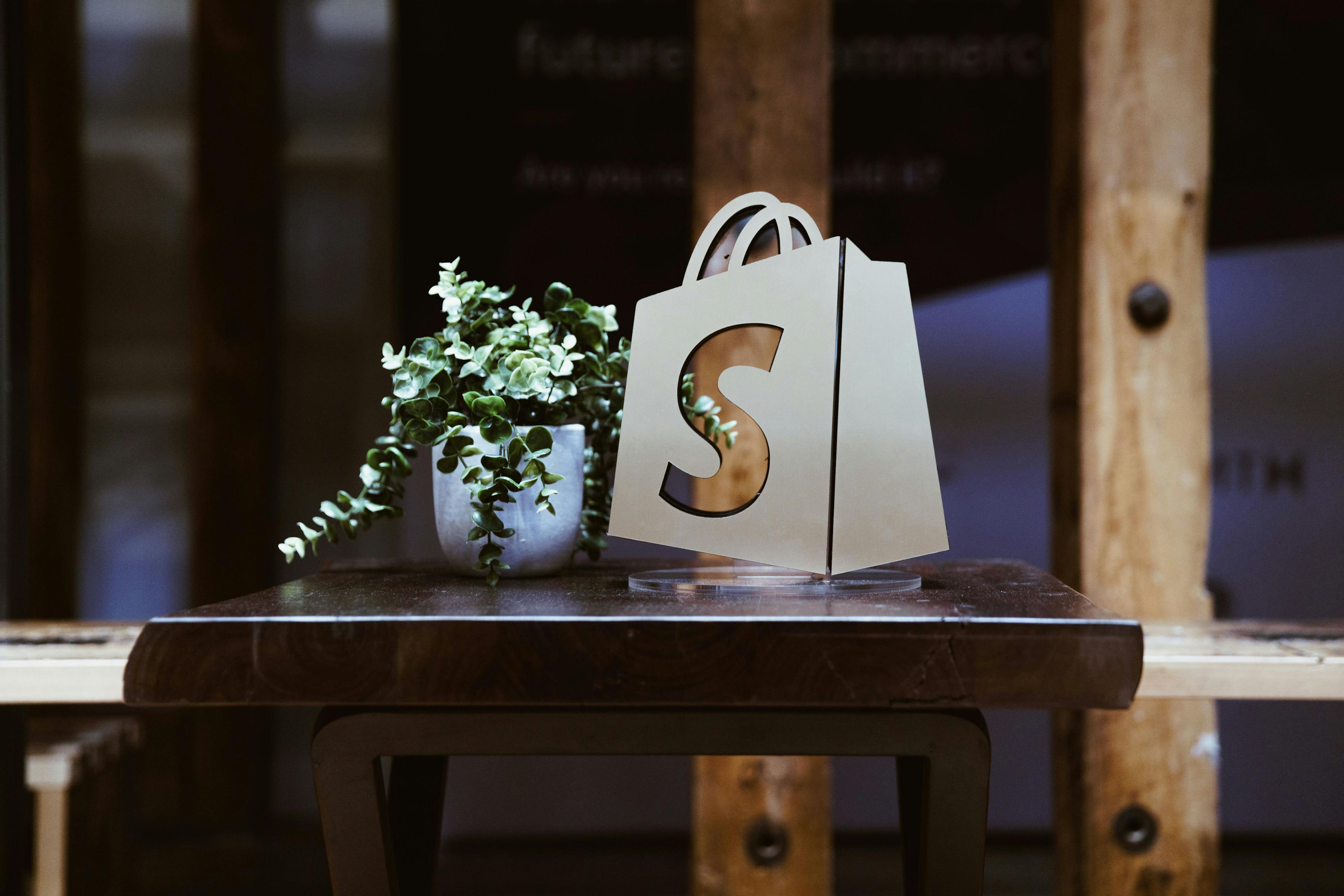 a logo of Shopify on a window in front of a table that could be used as a co-working space for Shopify merchants